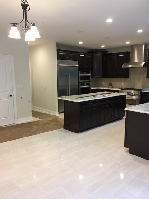 kitchen featuring a center island, wall chimney exhaust hood, hanging light fixtures, stainless steel appliances, and a notable chandelier