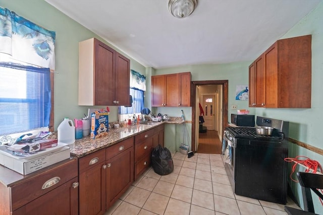 kitchen with light stone counters, brown cabinetry, light tile patterned flooring, and gas range