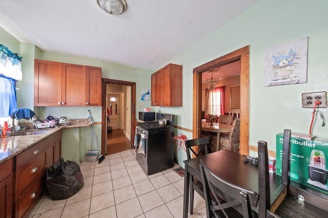 kitchen featuring light tile patterned floors, stainless steel gas range oven, brown cabinetry, and a sink