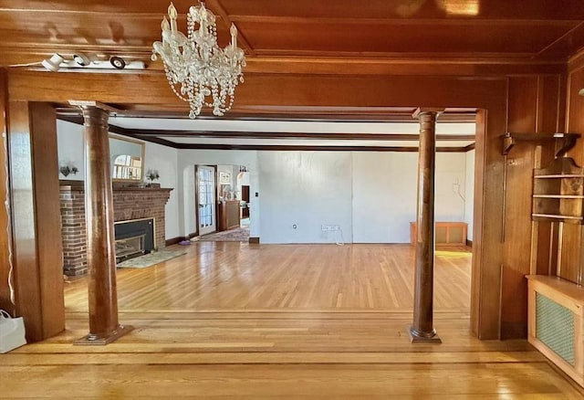 unfurnished living room featuring beamed ceiling, a brick fireplace, wood finished floors, and ornate columns