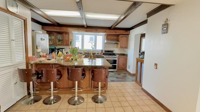 kitchen featuring a breakfast bar, appliances with stainless steel finishes, glass insert cabinets, beamed ceiling, and a peninsula