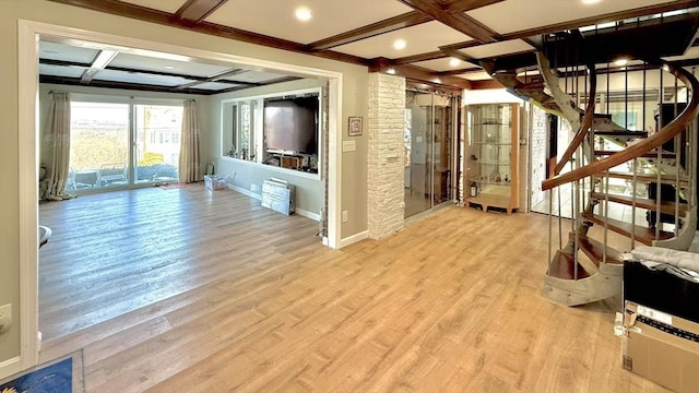 unfurnished living room with beam ceiling, light wood finished floors, coffered ceiling, baseboards, and stairs