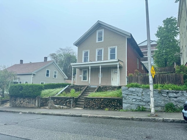 traditional-style house featuring a porch, stairway, and fence