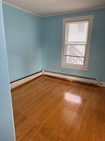 empty room with hardwood / wood-style flooring, baseboard heating, and crown molding