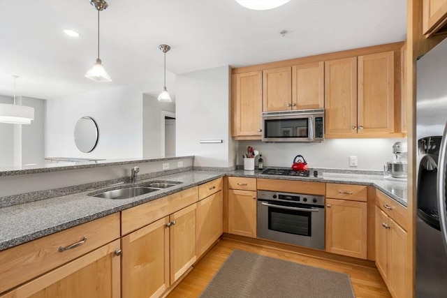 kitchen with light brown cabinetry, appliances with stainless steel finishes, a sink, and decorative light fixtures