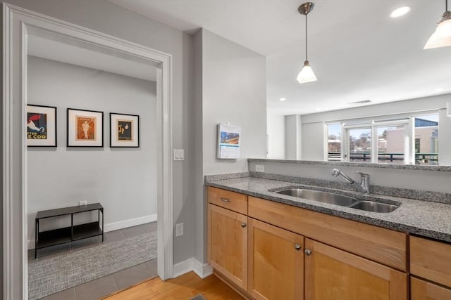 kitchen featuring baseboards, decorative light fixtures, a sink, and dark stone countertops