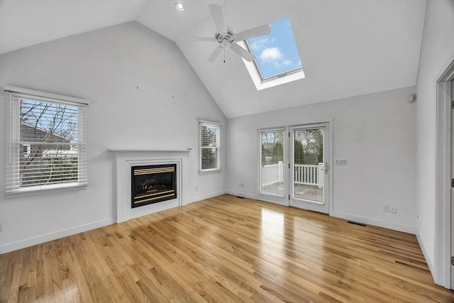 unfurnished living room featuring light hardwood / wood-style floors, vaulted ceiling with skylight, ceiling fan, and a wealth of natural light