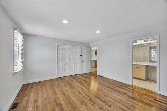 unfurnished bedroom with multiple windows, light wood-type flooring, and ensuite bath