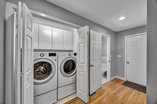 clothes washing area with cabinets, washing machine and clothes dryer, and light hardwood / wood-style flooring