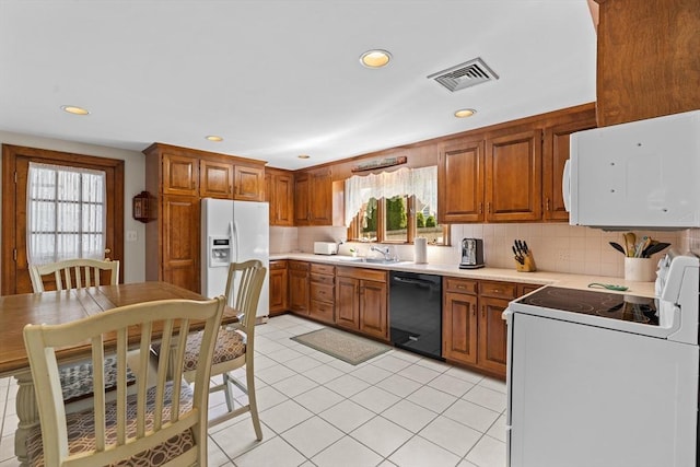 kitchen with a sink, brown cabinets, white appliances, and visible vents