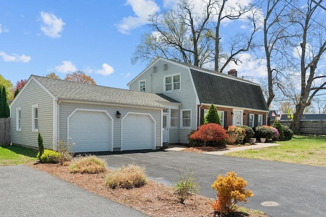 colonial inspired home featuring a shingled roof, an attached garage, a gambrel roof, aphalt driveway, and a chimney