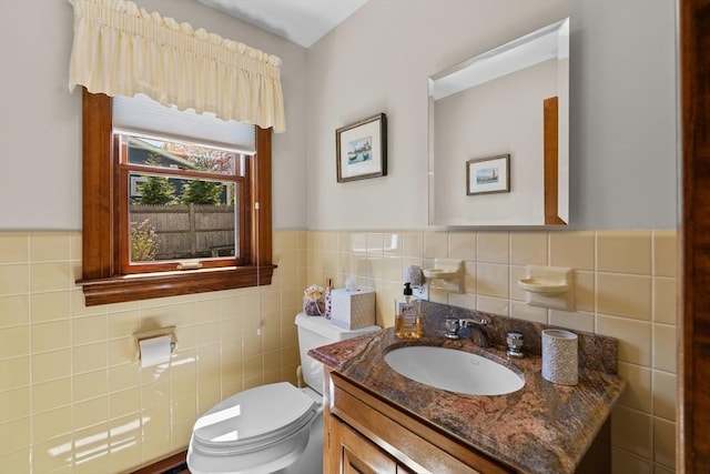 bathroom with toilet, tile walls, a wainscoted wall, and vanity