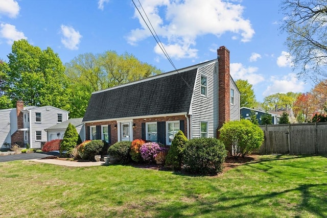 colonial inspired home with a shingled roof, fence, a front yard, and a chimney