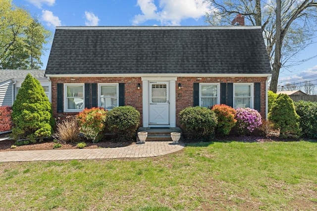 dutch colonial featuring brick siding, a shingled roof, a front lawn, and a chimney