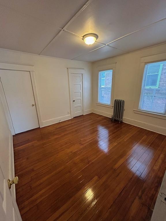 unfurnished bedroom featuring radiator heating unit, baseboards, and dark wood finished floors