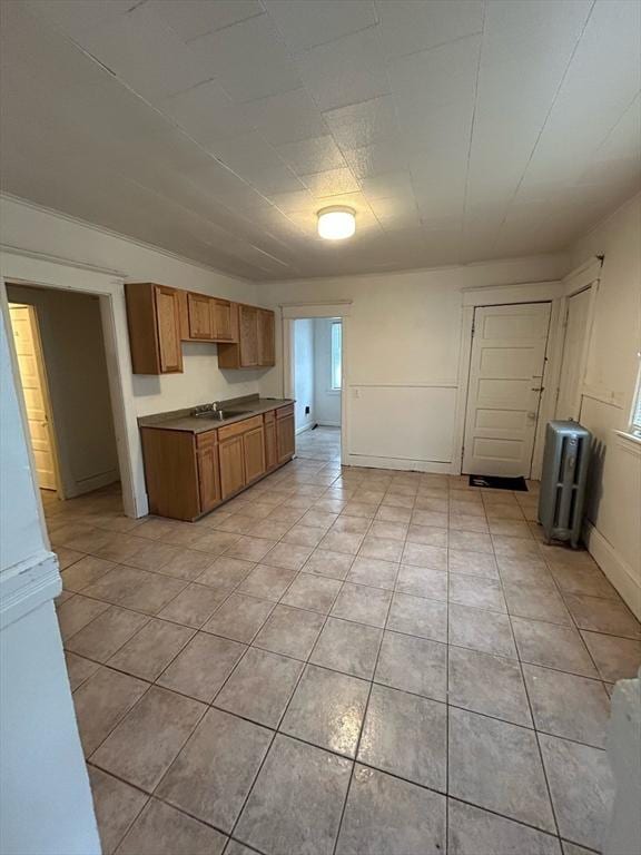 kitchen with light tile patterned flooring, a sink, baseboards, light countertops, and brown cabinetry