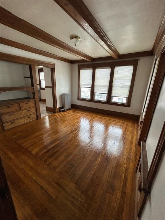 interior space featuring radiator, a healthy amount of sunlight, beamed ceiling, and wood finished floors