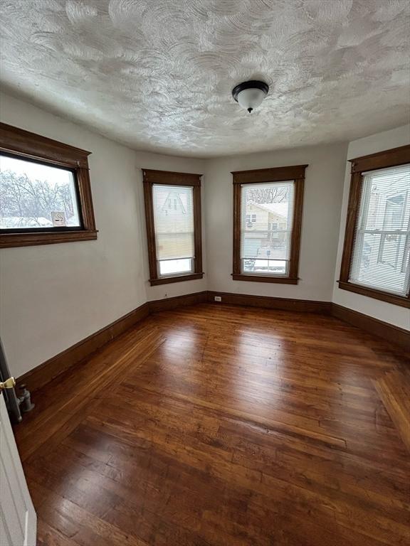 spare room with dark wood-style floors, baseboards, and a textured ceiling