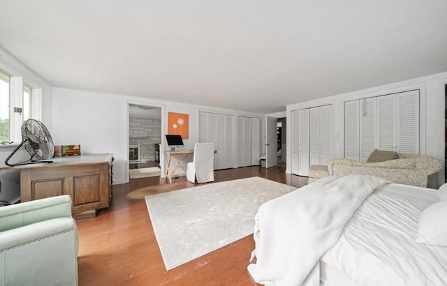 bedroom with a stone fireplace, two closets, and hardwood / wood-style flooring