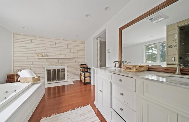 bathroom featuring hardwood / wood-style floors, vanity, a stone fireplace, and independent shower and bath