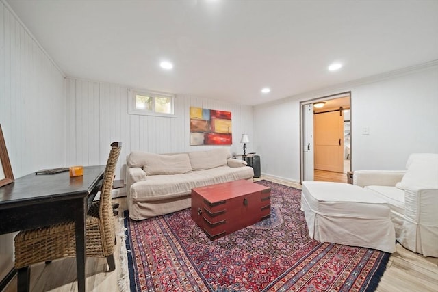 living room with a barn door, wooden walls, ornamental molding, and light wood-type flooring