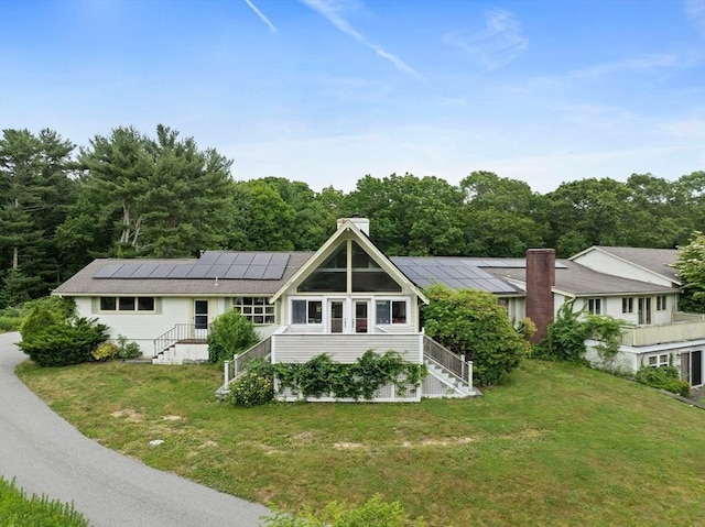 rear view of property with a lawn and solar panels