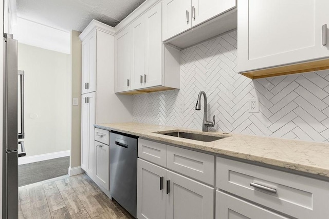 kitchen with sink, appliances with stainless steel finishes, white cabinetry, light stone counters, and decorative backsplash