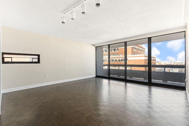 spare room featuring track lighting, dark parquet floors, a wall of windows, and a textured ceiling