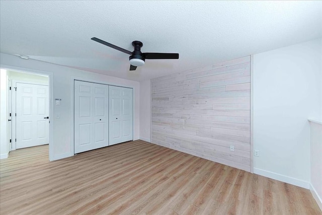 unfurnished bedroom with a textured ceiling, wooden walls, wood finished floors, a ceiling fan, and a closet