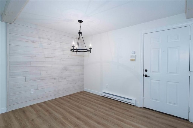 unfurnished dining area with a baseboard heating unit, a notable chandelier, wood walls, and wood finished floors