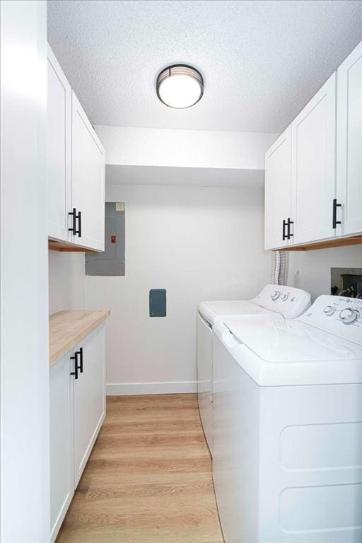 laundry area featuring cabinet space, electric panel, washer and clothes dryer, light wood-style flooring, and a textured ceiling