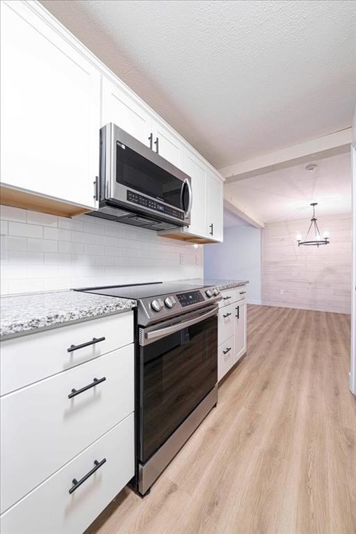 kitchen with light wood-style flooring, white cabinetry, stainless steel appliances, and a textured ceiling