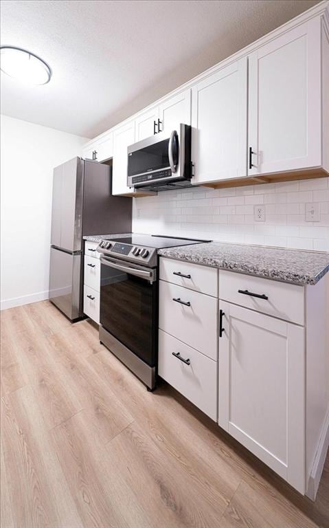 kitchen with white cabinets, light wood-style flooring, appliances with stainless steel finishes, and tasteful backsplash