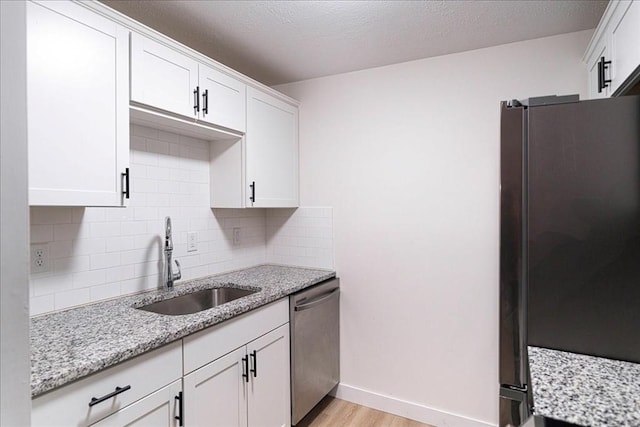 kitchen with light wood finished floors, white cabinets, dishwasher, freestanding refrigerator, and a sink