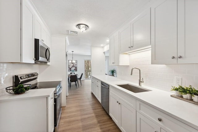 kitchen with white cabinetry, appliances with stainless steel finishes, decorative backsplash, sink, and light hardwood / wood-style flooring