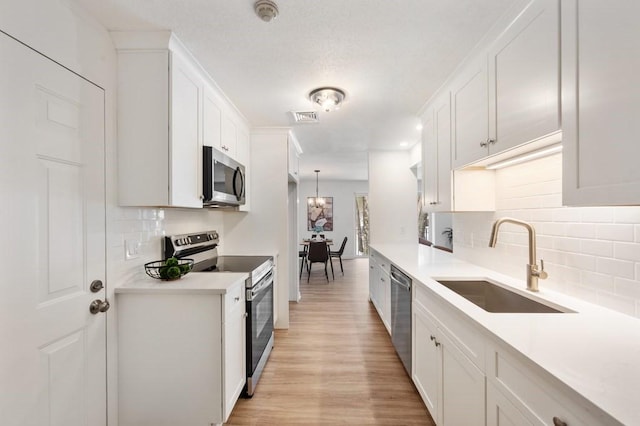 kitchen featuring white cabinets, stainless steel appliances, decorative light fixtures, and sink