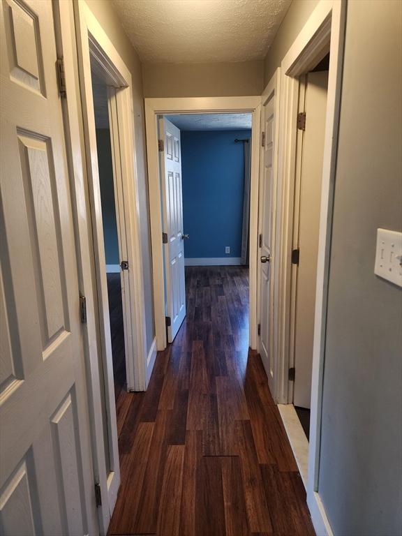 hall featuring a textured ceiling, dark wood-type flooring, and baseboards