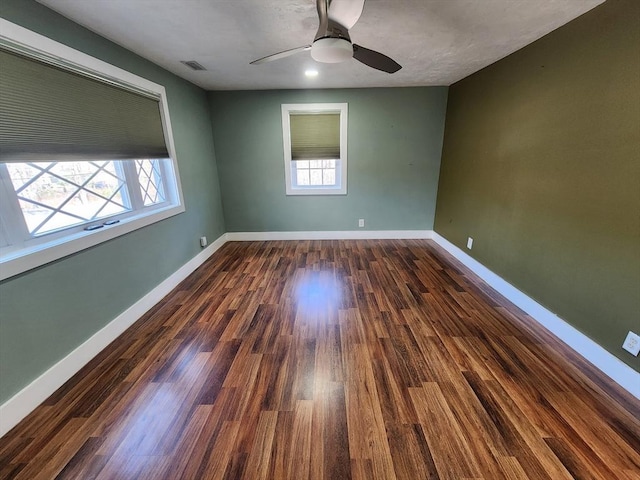 empty room with dark wood-style floors, visible vents, and baseboards