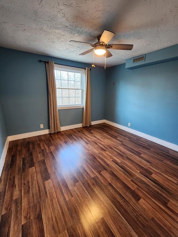 spare room featuring visible vents, ceiling fan, baseboards, wood finished floors, and a textured ceiling