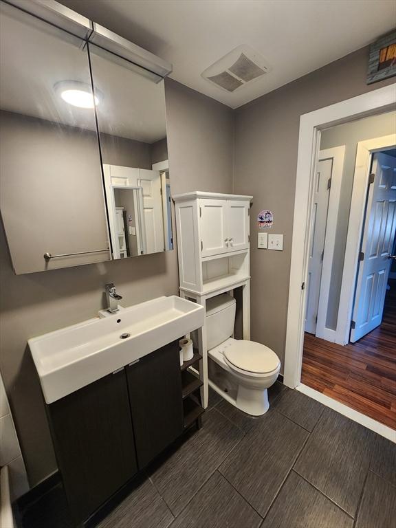 bathroom featuring wood finish floors, visible vents, toilet, and vanity