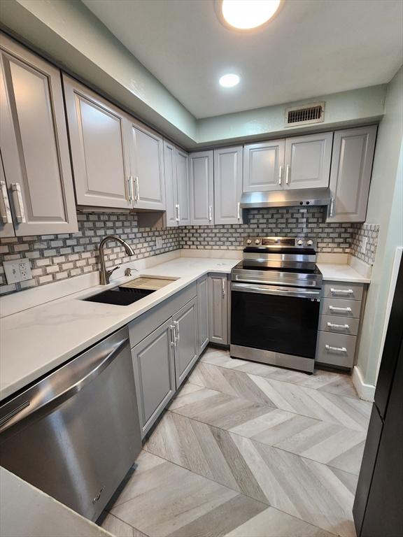 kitchen with light countertops, decorative backsplash, gray cabinets, stainless steel appliances, and a sink