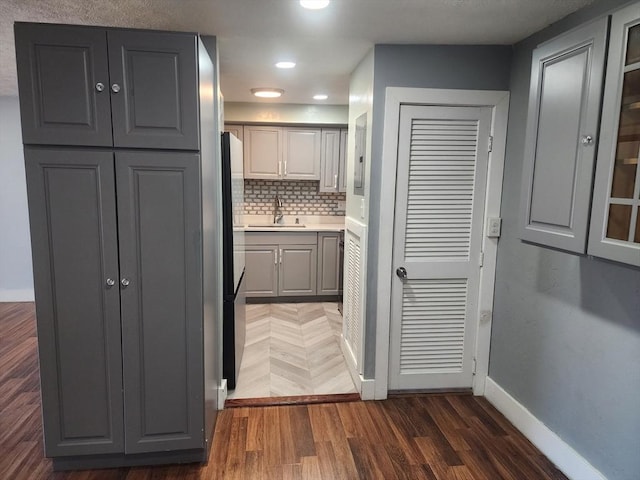 kitchen featuring gray cabinetry, a sink, wood finished floors, decorative backsplash, and baseboards