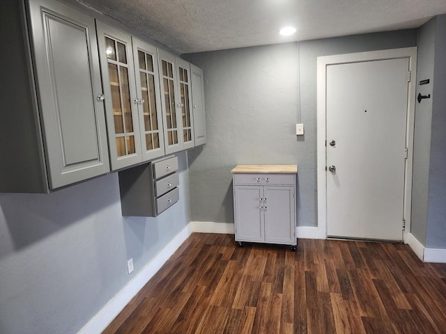 interior space with a textured wall, a textured ceiling, baseboards, and dark wood-style flooring