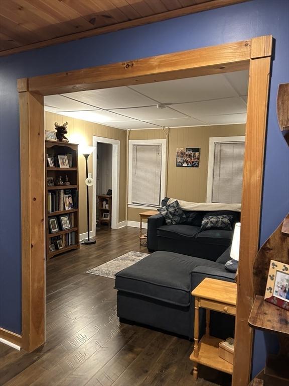 living area featuring beamed ceiling, wood finished floors, and wooden walls