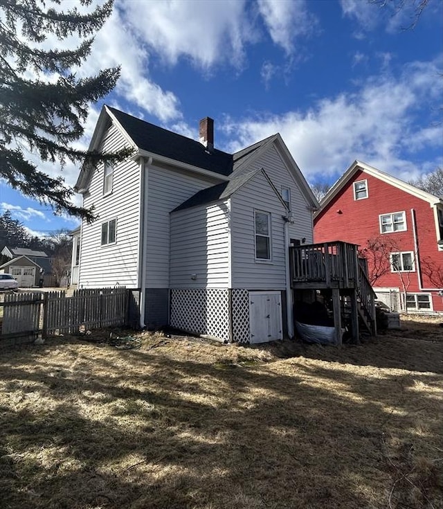 back of house featuring a lawn, a chimney, stairs, fence, and a deck