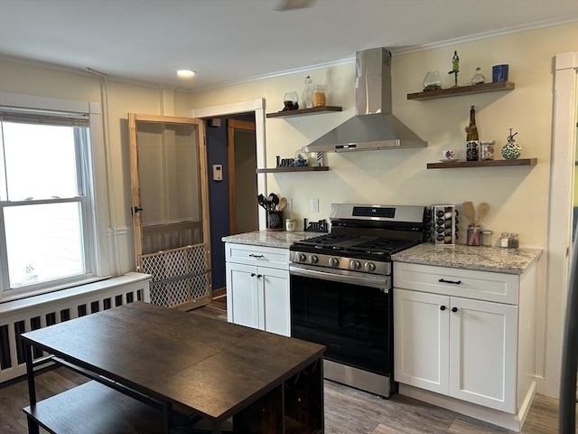 kitchen featuring stainless steel gas range oven, radiator heating unit, wall chimney exhaust hood, white cabinetry, and open shelves