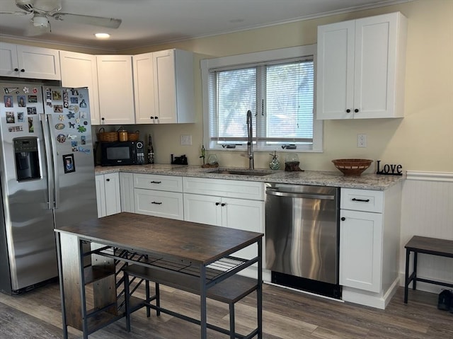 kitchen featuring white cabinets, dark wood finished floors, wainscoting, stainless steel appliances, and a sink