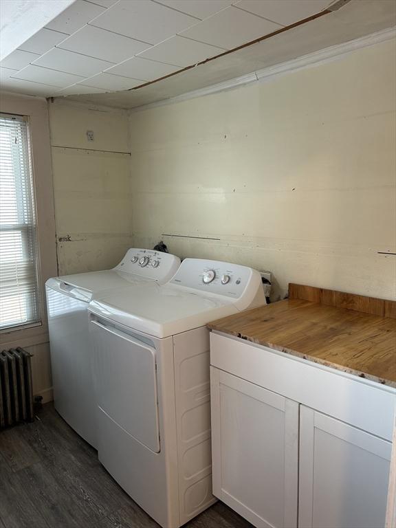 clothes washing area with washer and clothes dryer, dark wood finished floors, cabinet space, and radiator