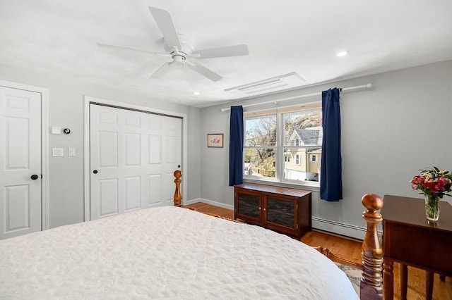 bedroom featuring wood finished floors, baseboards, a baseboard heating unit, and a closet