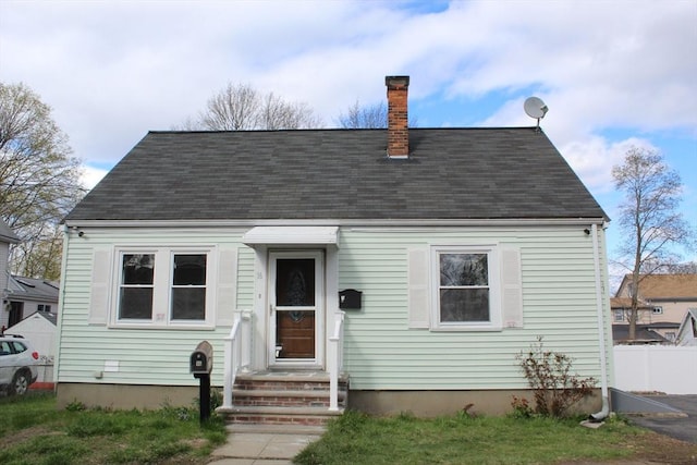 cape cod home featuring roof with shingles, a chimney, and fence